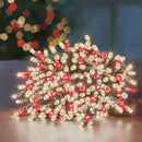 A pile of red and white LED holiday string lights glowing on a reflective surface with a blurred festive background.