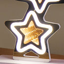 A star-shaped decorative light with a reflective silver frame, glowing white outer border, and warm gold inner star, shown lit against a neutral indoor background.