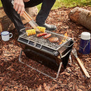 Portable grill with food being cooked outdoors on a natural ground surface.